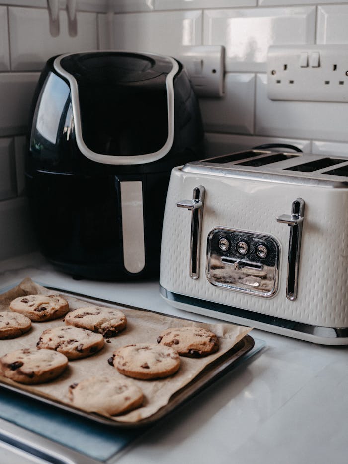Freshly baked cookies on tray beside air fryer and toaster.