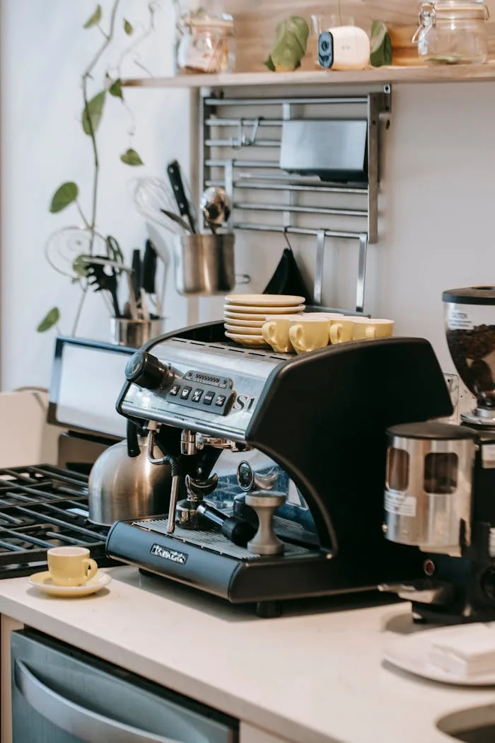 Coffee maker with portafilter placed in kitchen with shelves ceramic cups stove and cutlery